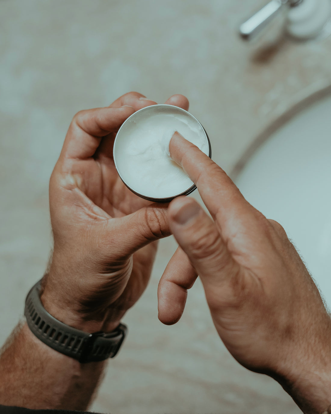 person scooping tallow balm out of a tin to use on the face or hands or body